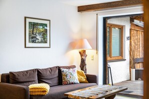 A living room with a sofa, a lamp, a framed picture, and a wooden table. - Apartment 'Am Wehr' with Mountain View, Private Terrace and Wi-Fi (Garmisch-Partenkirchen)