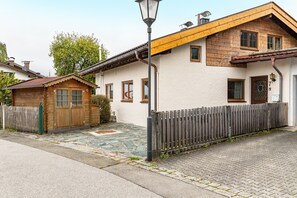 A two-story house with a wooden exterior, a stone-paved entrance, and a metal fence. - Apartment 'Am Wehr' with Mountain View, Private Terrace and Wi-Fi (Garmisch-Partenkirchen)