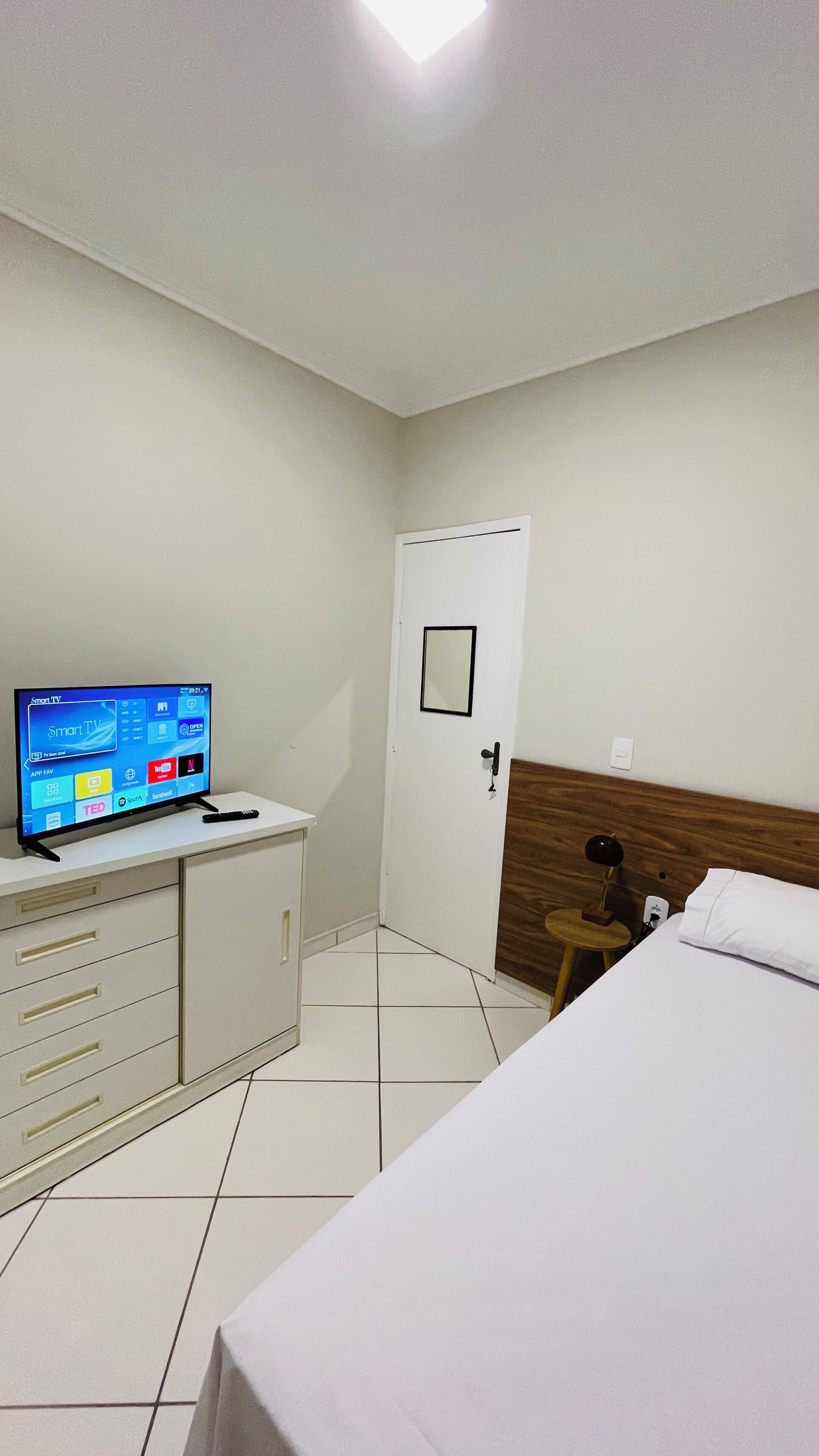 A hotel room with a bed, a TV on a cabinet, a door, and a wooden headboard.