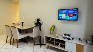Un salon moderne comprenant un coin repas, un téléviseur à écran plat fixé au mur et un sol carrelé de couleur blanche.