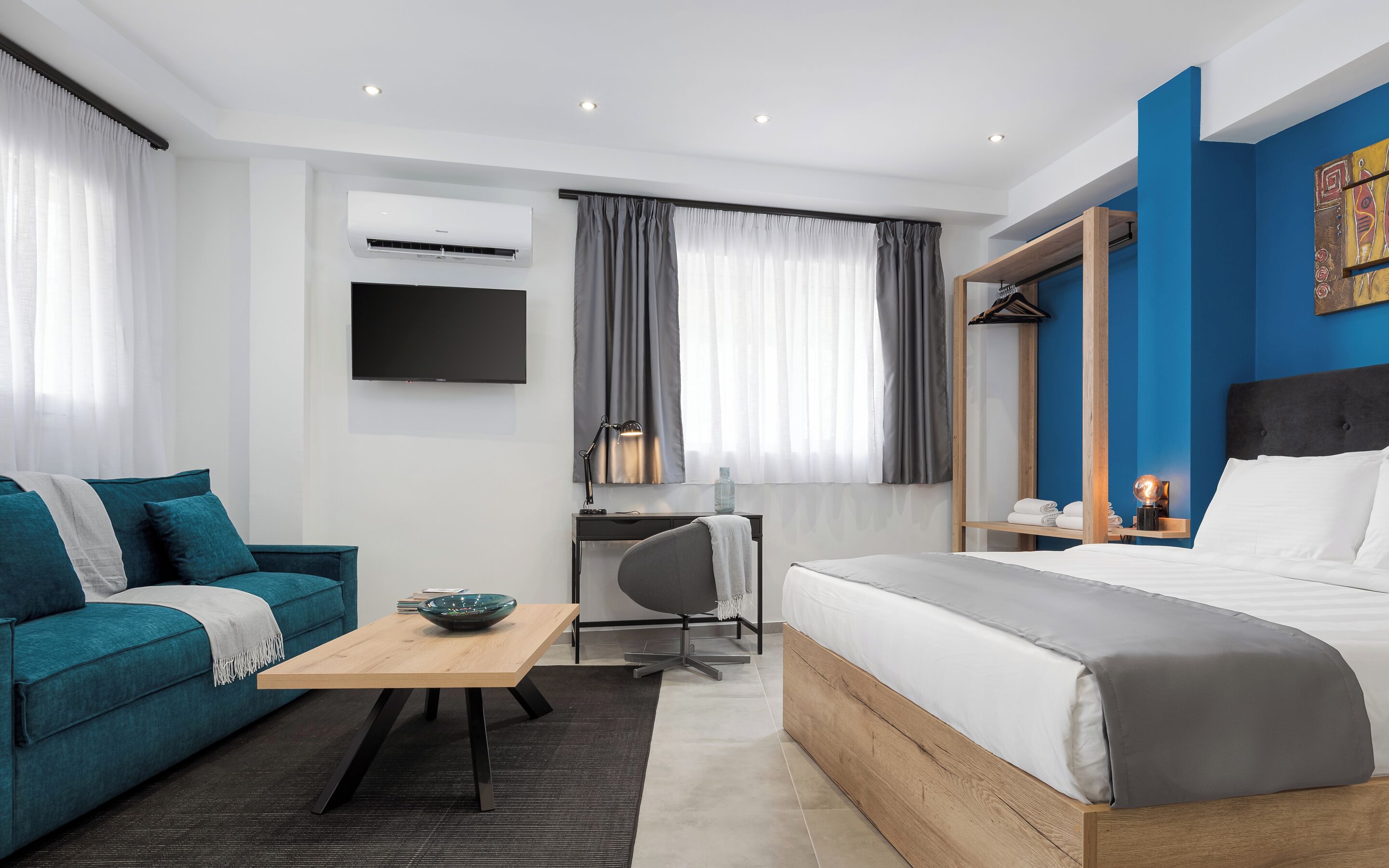 A modern hotel room with a bed, a sofa, a desk, and a TV.
