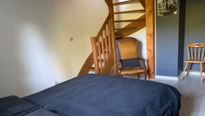 A bedroom with a large bed, a wooden chair, a wooden chair with a cushion, and a staircase.