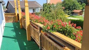 Una terraza de madera con césped artificial verde, rodeada de barandas de madera y flores rojas.