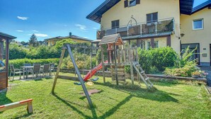 A residential area with a playground, a dining table with chairs, and a two-story house with a balcony. - Apartment 'Seenähe' with Shared Terrace, Shared Garden and Wi-Fi (Mattsee)