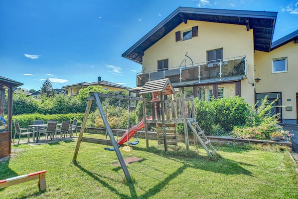 A residential area with a playground, a dining table with chairs, and a two-story house with a balcony.