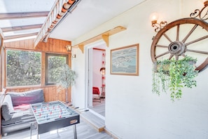 A cozy room with a foosball table, wooden beams, a large wheel wall decoration, and a hanging plant.
