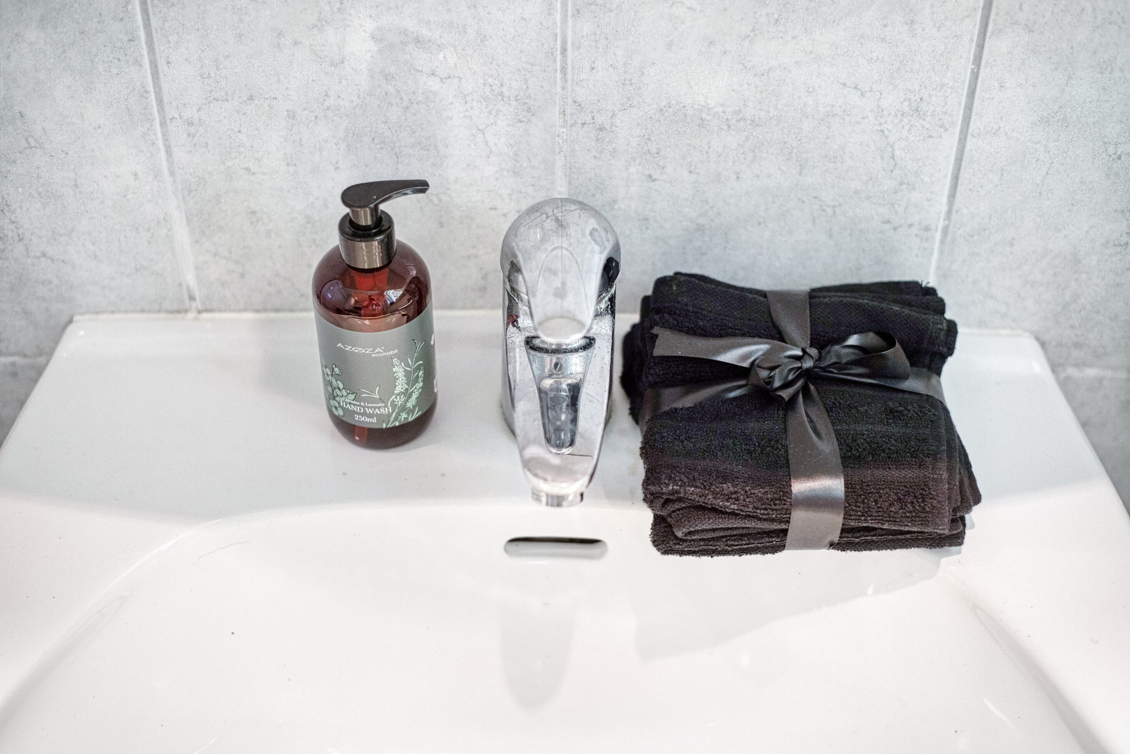 A bathroom sink with a hand soap dispenser, a faucet, and a towel.