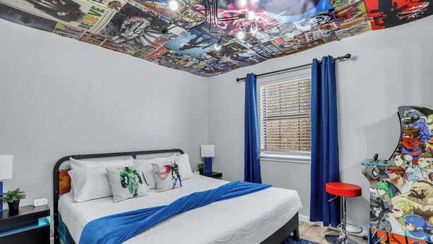 Ein Schlafzimmer mit einem Bett, einem Schreibtisch, einem Stuhl, einem Fenster mit Vorhängen und einer Decke mit einer Comic-Wandmalerei.