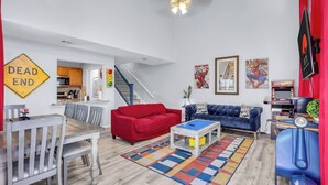 Ein Wohnzimmer mit einem roten Sofa, einem blauen Sofa, einem Esstisch mit Stühlen, einem Couchtisch und einem bunten Teppich.