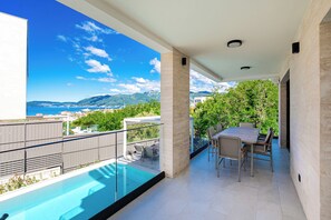 Uma varanda com piscina, área de estar ao ar livre e vista para o mar e montanhas.