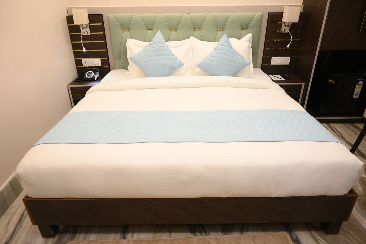 A neatly made bed with a quilted headboard, a bedside table with a lamp, and a nightstand with a camera.