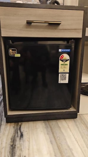 A black refrigerator with a 5-year warranty sticker, a Blue Star Energy Savings label, and a QR code.