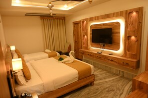A hotel room with a large bed, a TV mounted on a wooden panel, and a bedside table with a lamp. - Hotel Kashi Crown (Varanasi)