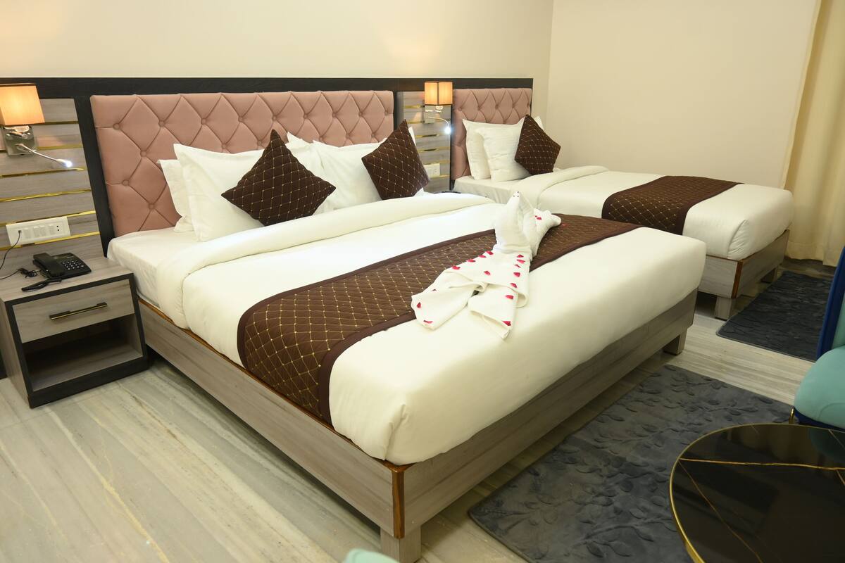 A hotel room with two beds, each with white linens and brown accents, a nightstand with a phone and lamp, and a small table with a chair.