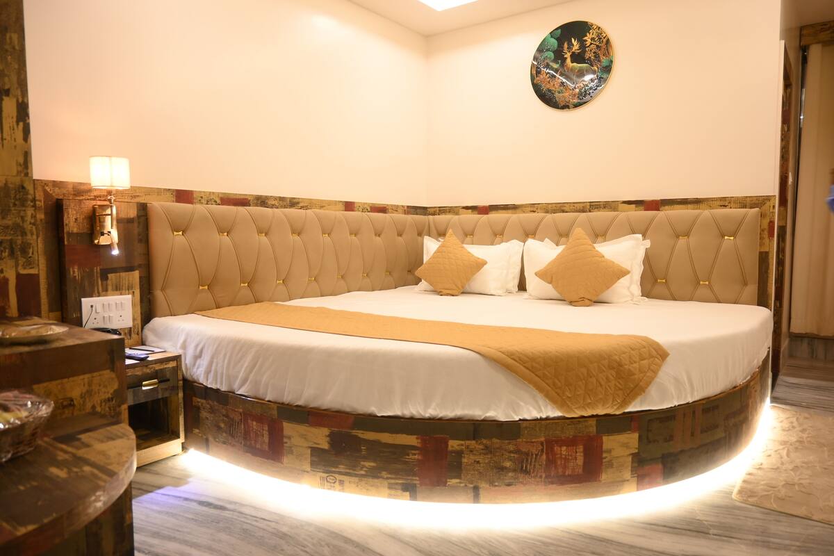 A circular bed with a tufted headboard, a bedside table with a lamp, and a decorative wall piece.