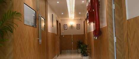 Un pasillo de hotel con paneles de madera, suelo de mármol y techo con una lámpara de diseño.