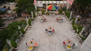 An outdoor terrace with multiple tables and chairs, surrounded by potted plants and string lights. - Hotel Kashi Crown (Varanasi)