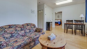 Uma sala de estar com um sofá estampado, uma mesa de centro de madeira e uma área de jantar com cadeiras e uma mesa.