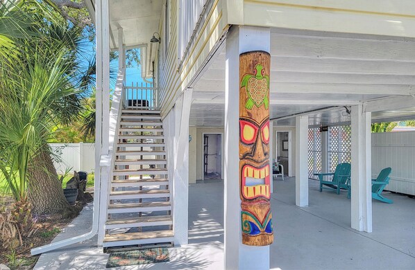 A covered outdoor area with a wooden post featuring a turtle design, a wooden staircase, and green chairs. - Quaint Coastal Cottage Just Steps To The Sparkling Gulf Waters (Indian Rocks Beach)