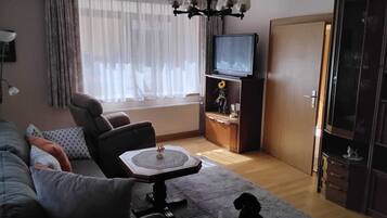 A living room with a sofa, armchair, coffee table, TV, and a cabinet with a flower vase.
