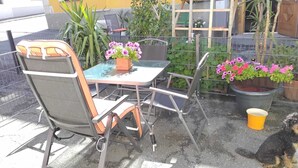 Un patio con tavolo e sedie, piante in vaso e un secchio giallo.