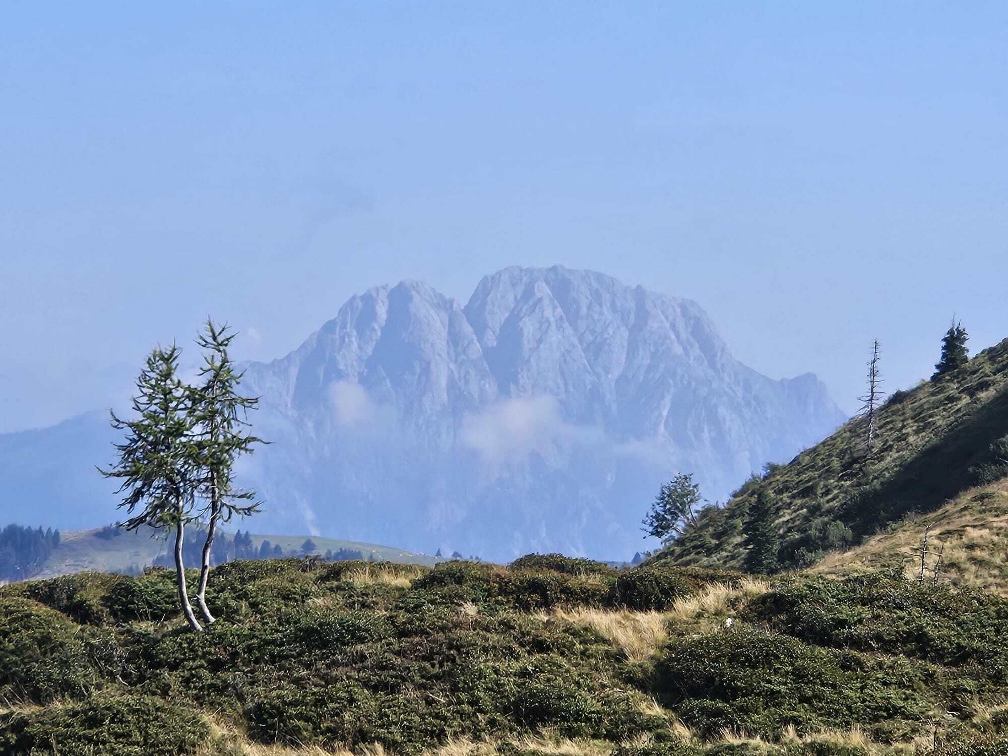 A mountainous landscape with a prominent peak, sparse vegetation, and a clear sky.
