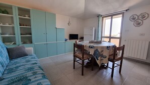 Een compacte leefruimte met een eettafel, stoelen, een bank en een kitchenette.