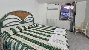 Een opgemaakt bed met een gestreept dekbedovertrek, een houten stoel en een raam met uitzicht op een heuvel.