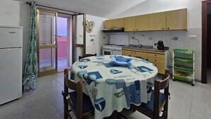 Een compacte keuken met een tafel bedekt met een blauw-witte tafelkleed, houten keukenkastjes, een fornuis en een koelkast.