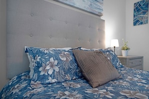 A bed with floral bedding, a tufted headboard, a bedside table with a lamp, and a plant.