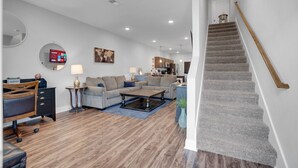 A modern living room with a staircase, wooden flooring, and a kitchen in the background.