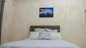 Un dormitorio con cama, cabecera y un cuadro de un barco en el agua.