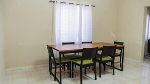Un comedor con una mesa de madera y seis sillas, una ventana con cortinas blancas y un piso de baldosas.