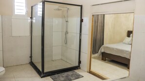 Un baño con ducha de vidrio, inodoro y cama con cortina.