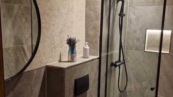 Un baño moderno con un espejo redondo, un lavamanos negro, un inodoro y una ducha con mampara de vidrio.