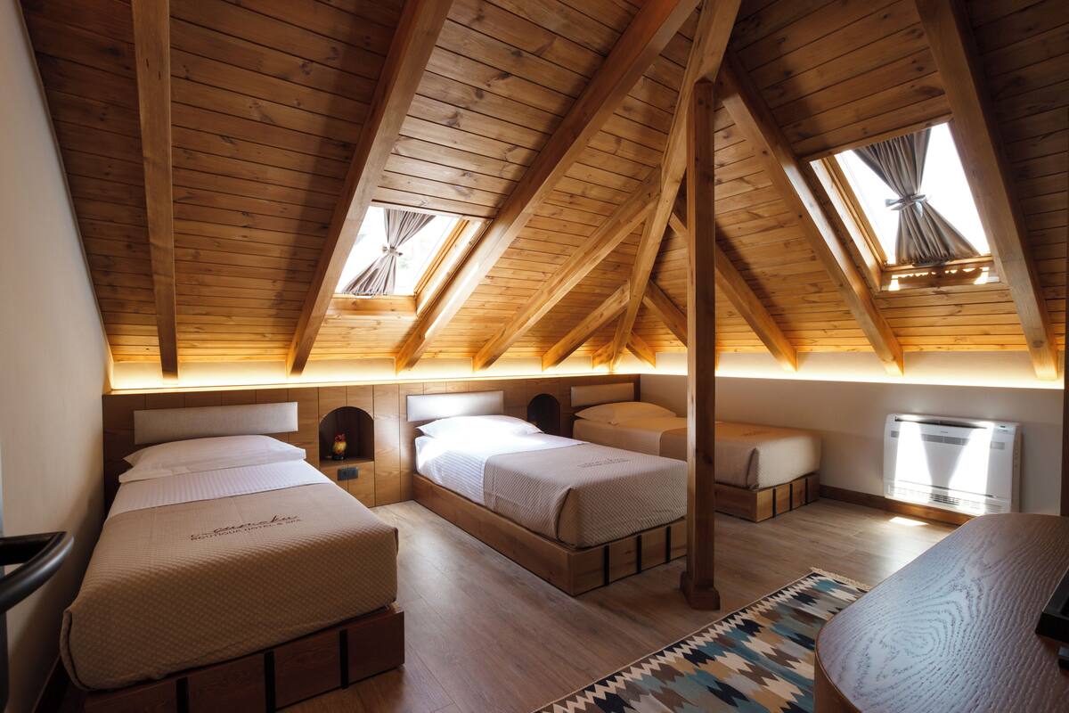A bedroom with two beds, wooden beams, skylights, and a window with curtains.
