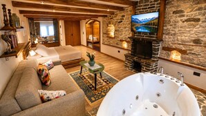 A cozy room with a sofa, a large bathtub, a stone fireplace, and a television. - Cumaku Boutique Hotel & Spa (Gjirokastër)