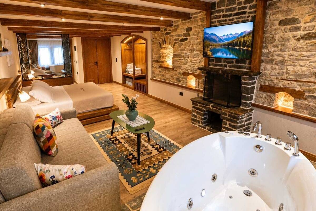 A cozy room with a sofa, a large bathtub, a stone fireplace, and a television.