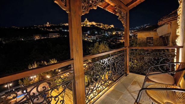 A balcony with ornate metal railings, a wicker chair, and a view of a cityscape at night. - Cumaku Boutique Hotel & Spa (Gjirokastër)