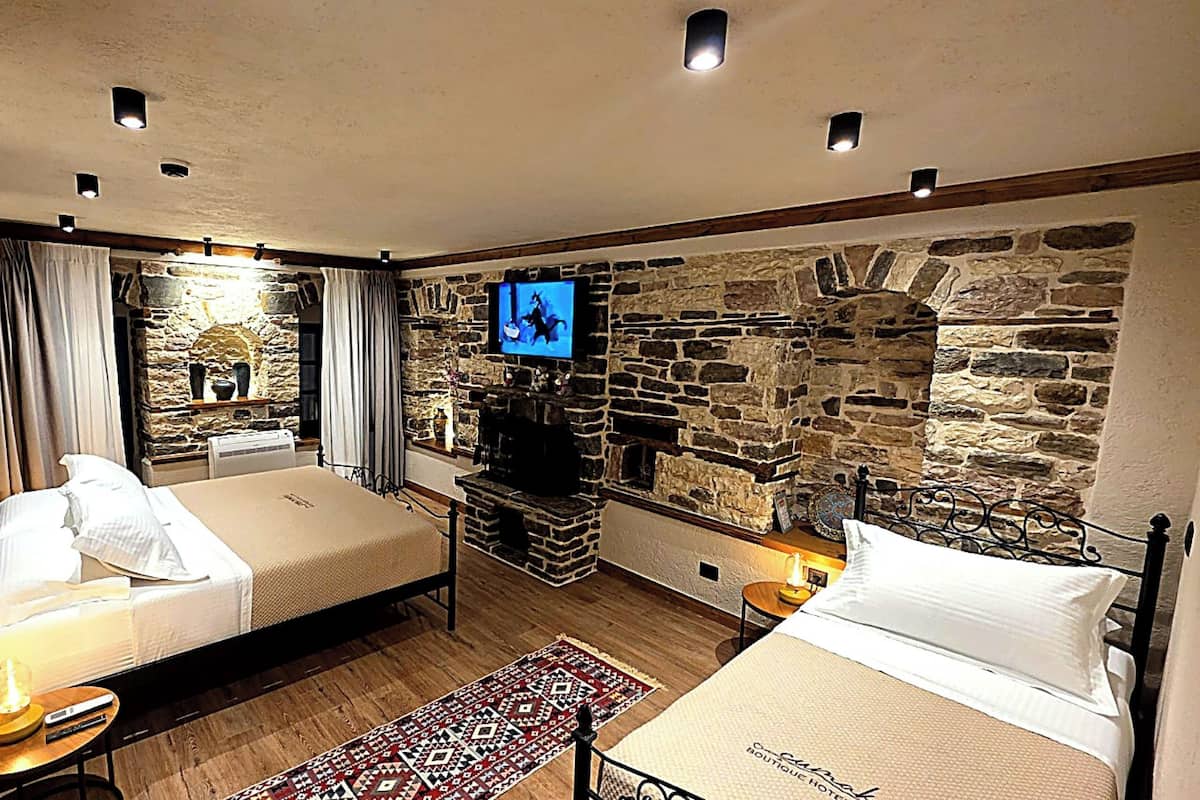 A room with two beds, a stone wall, a fireplace, and a television.