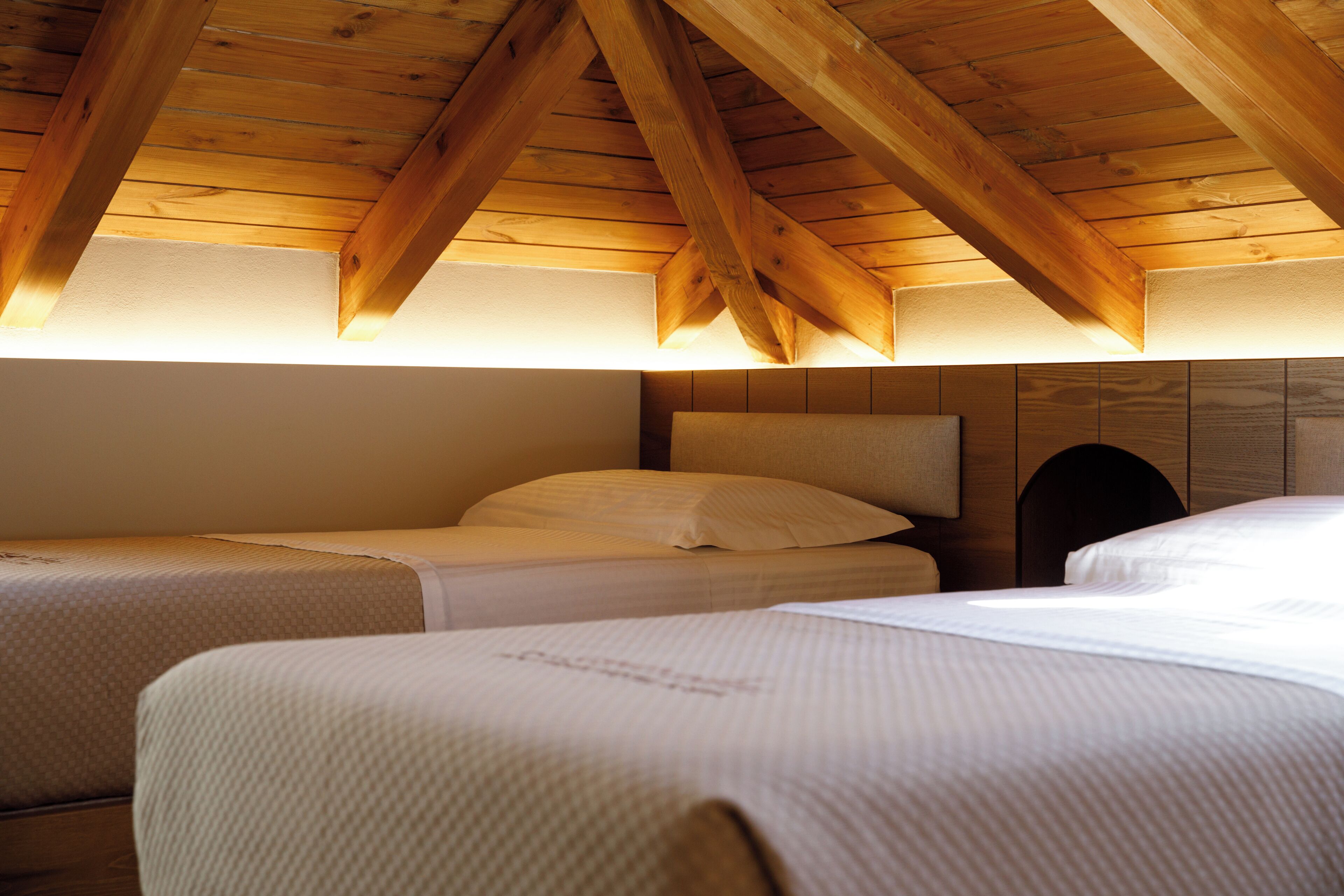 A room with two beds, wooden beams on the ceiling, and a headboard with a built-in shelf.