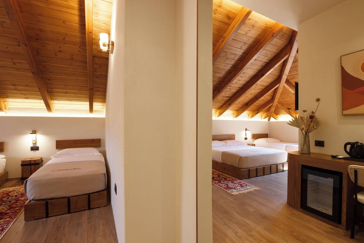 A bedroom with two beds, wooden ceiling beams, a small desk with a chair, and a decorative vase.