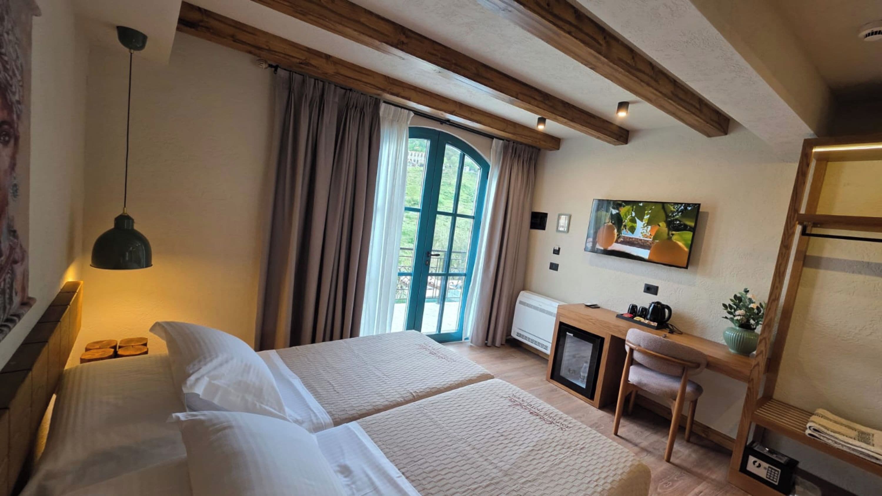 Une chambre à coucher comprenant un lit, une table de chevet, un bureau, une chaise, une télévision et une fenêtre avec des rideaux.