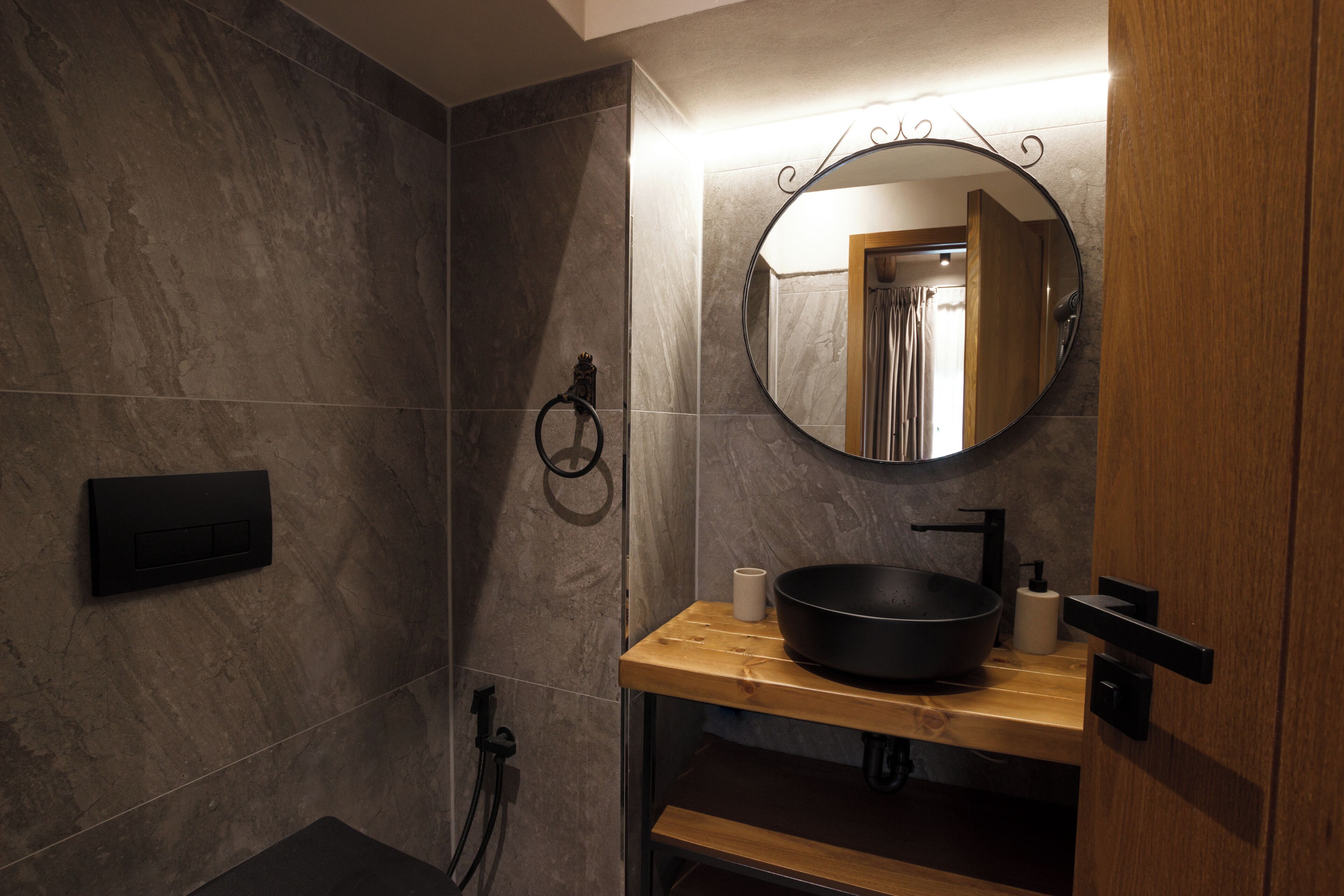 A modern bathroom with a wooden vanity, a black sink, and a large mirror.