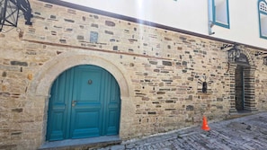 A stone building with a teal door, a cobblestone street, and a small orange cone. - Cumaku Boutique Hotel & Spa (Gjirokastër)