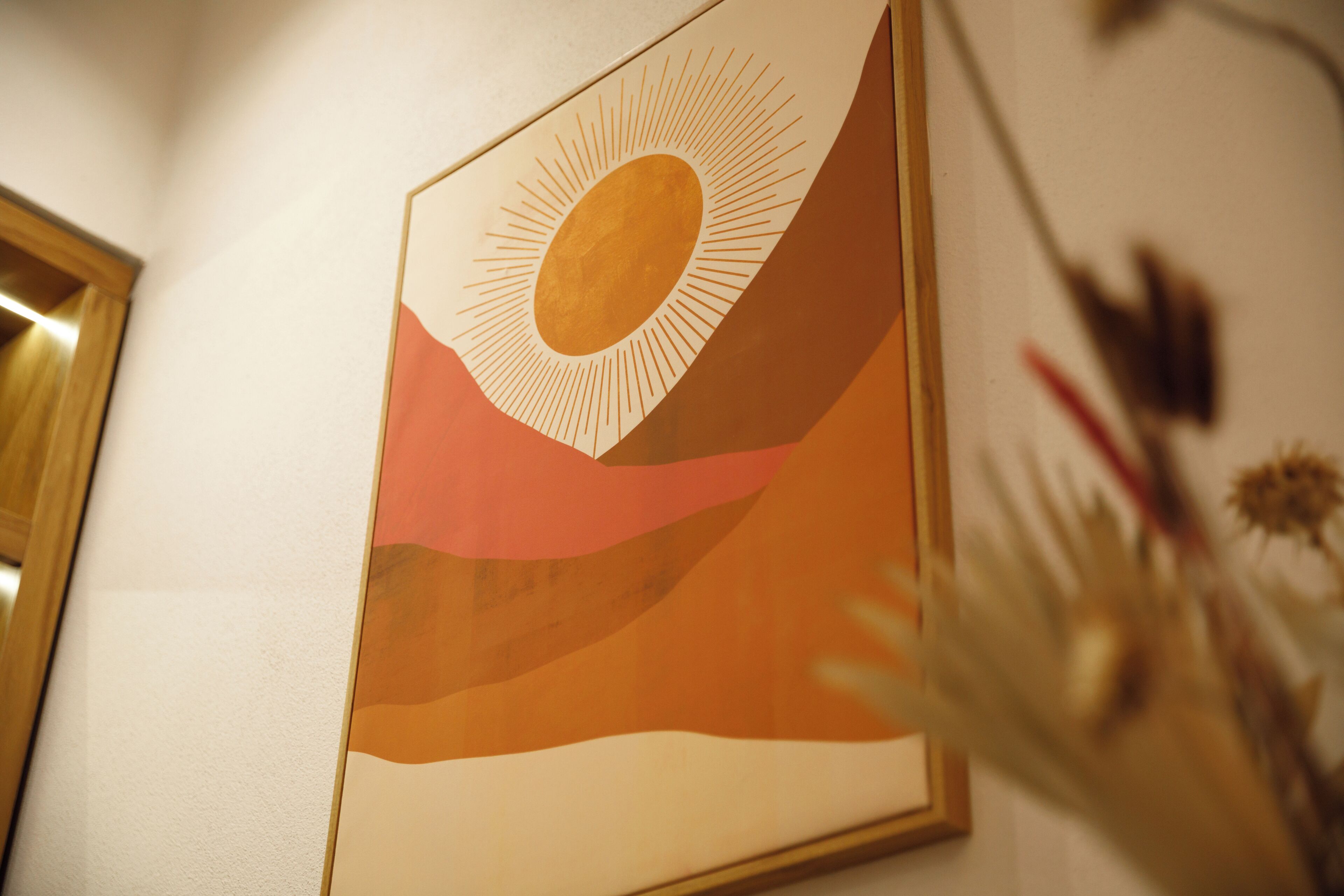 Un cuadro abstracto enmarco con un sol y un paisaje en una pared.