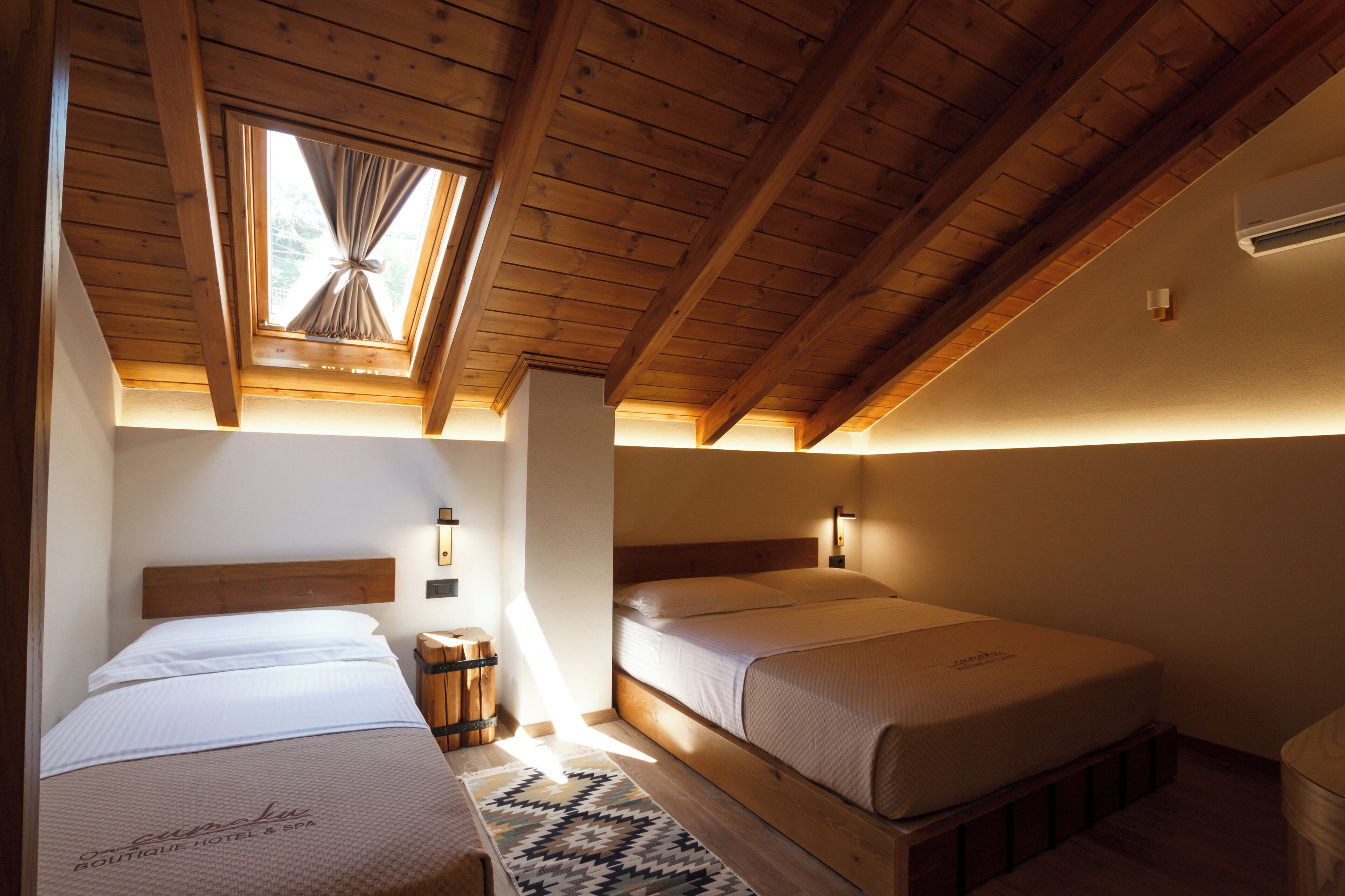 A room with two beds, wooden beams, a skylight, and a small rug.