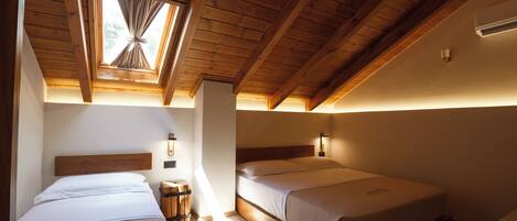 A room with two beds, wooden beams, a skylight, and a small rug.