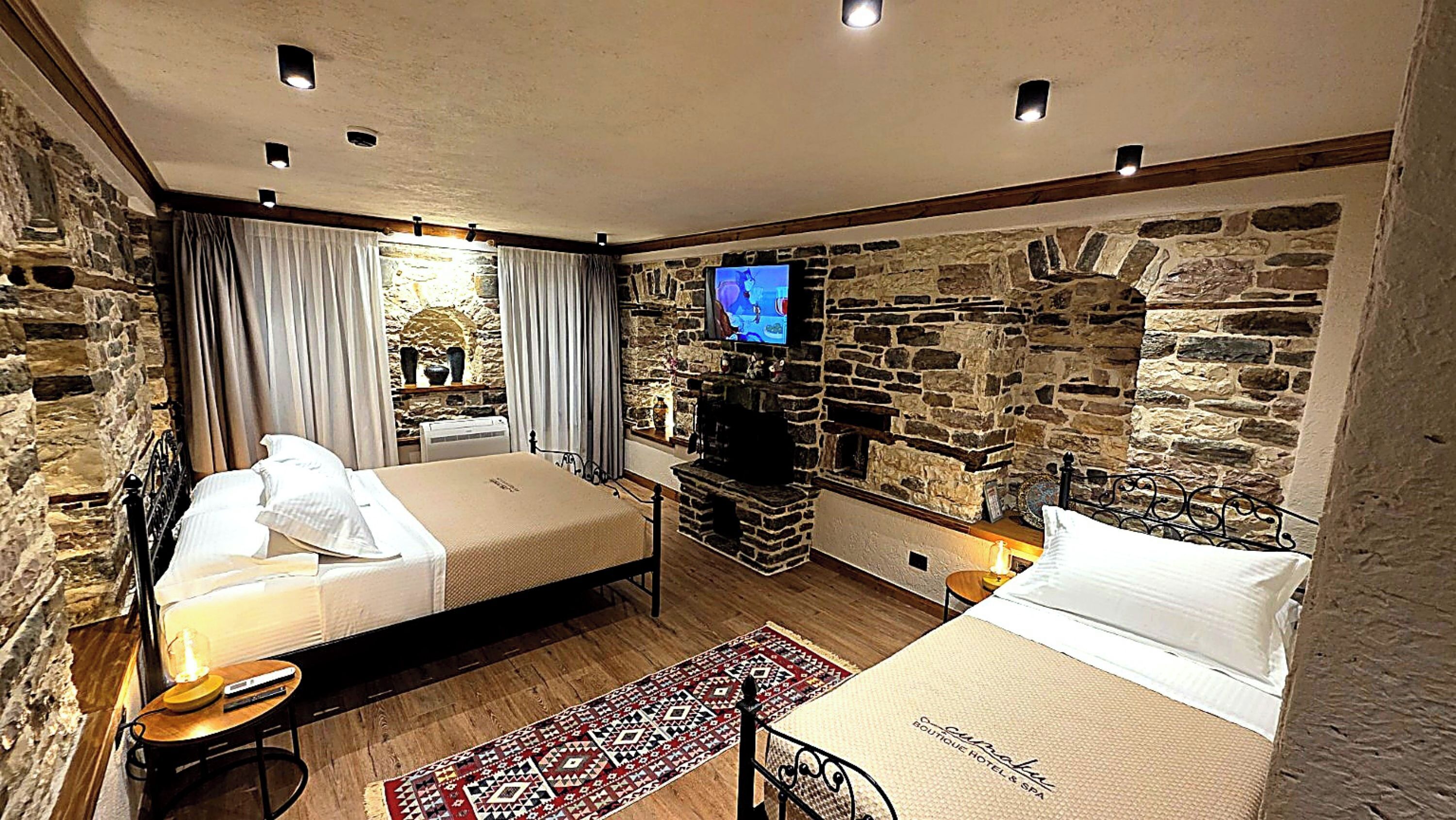 A room with two beds, a stone wall, a television, and a fireplace.