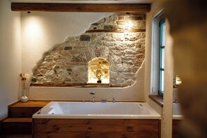A bathroom with a stone wall, a wooden bench, and a bathtub. - Cumaku Boutique Hotel & Spa (Gjirokastër)